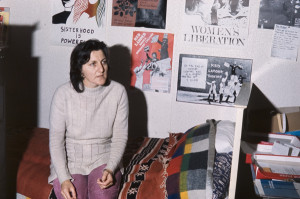 Ellen Malos sits on the bed in the women's centre. Women's Liberation posters adorn the walls
